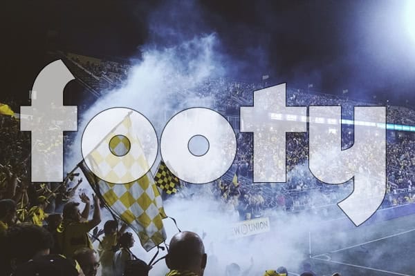 A football stadium crowd with smoke flares and flags, overlaid with the word 'footy'