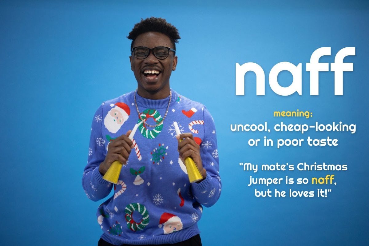 A young man laughs in a cheesy Christmas jumper covered in Santas and snowflakes, holding party horns. Text: naff, meaning uncool, cheap-looking or in poor taste. Example: My mate's Christmas jumper is so naff, but he loves it!